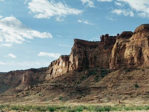 A panoramic view of a large, sunlit rock formation stretching across a vast, arid landscape under a partly cloudy blue sky. new features and premium plans on the horizon.