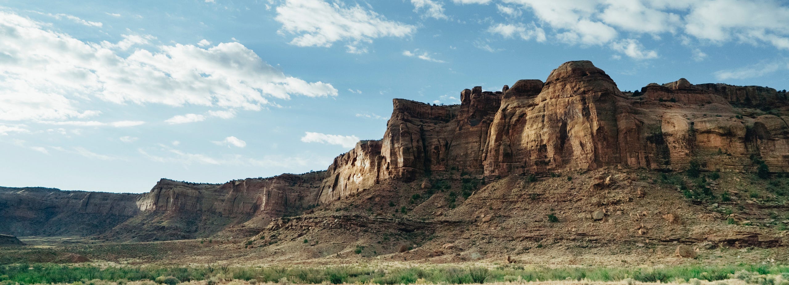 A panoramic view of a large, sunlit rock formation stretching across a vast, arid landscape under a partly cloudy blue sky. new features and premium plans on the horizon.