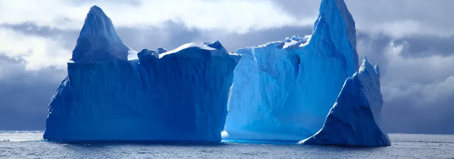 A panoramic photograph of massive, deep blue icebergs floating on the ocean under a dramatic and cloudy sky. MapHub's new Multi-Select tool.
